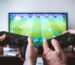 Close-up of hands holding gaming controllers in front of a TV. Engaged in a video gaming session.